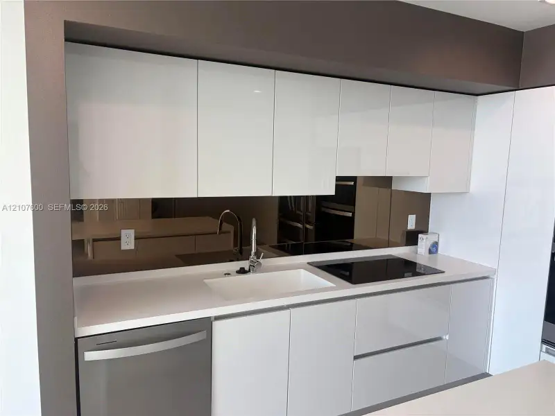 High-gloss cabinetry, integrated cooktop, undermount sink, solid surface countertop, and reflective backsplash