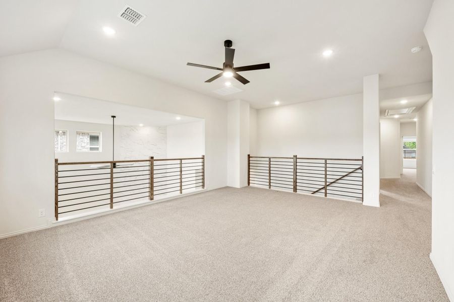 Open upstairs loft with carpet, ceiling fan, and metal horizontal stair railings along open edges Open upstairs loft with carpet, ceiling fan, and metal horizontal stair railings along open edges