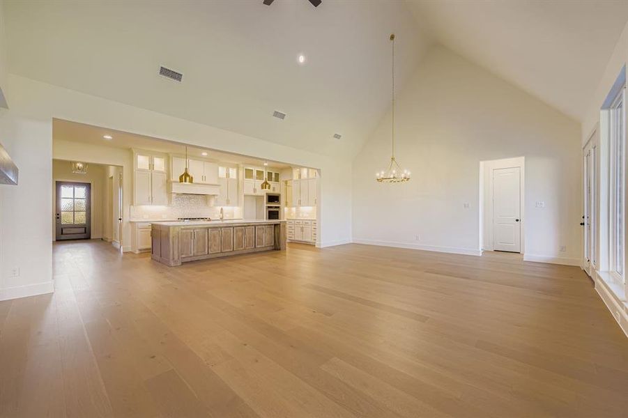 Unfurnished living room with high vaulted ceiling, a chandelier, light wood-type flooring, and recessed lighting