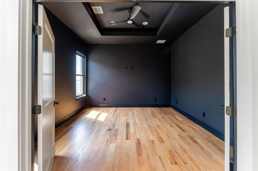 Spare room with a tray ceiling, wood finished floors, and ceiling fan