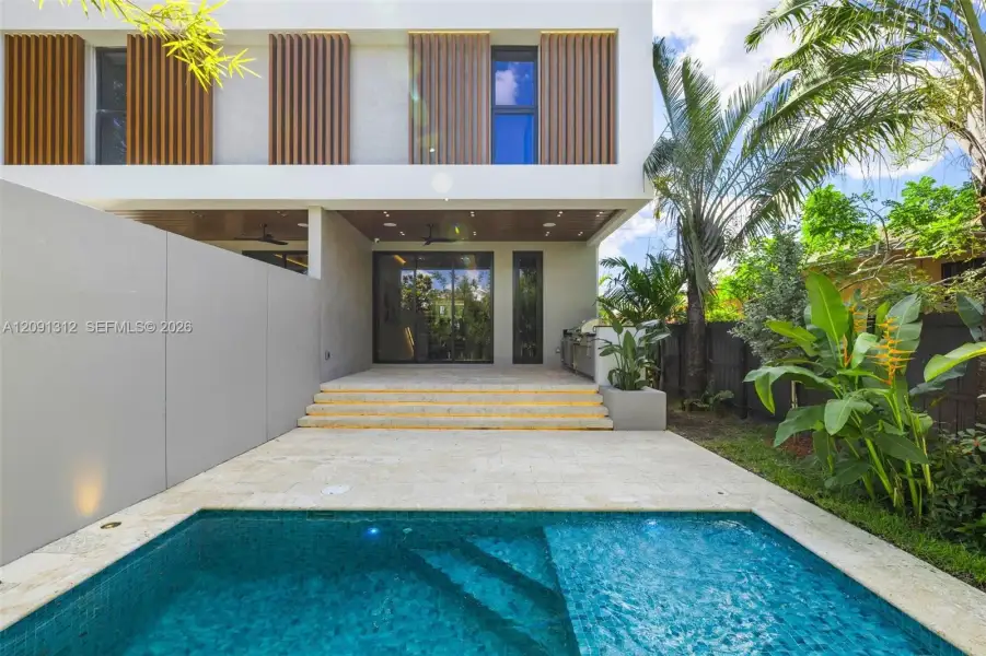 Modern exterior featuring vertical wood-slat privacy screens, stone patio with tiered steps, built-in outdoor kitchen, and a tiled swimming pool Modern exterior featuring vertical wood-slat privacy screens, stone patio with tiered steps, built-in outdoor kitchen, and a tiled swimming pool