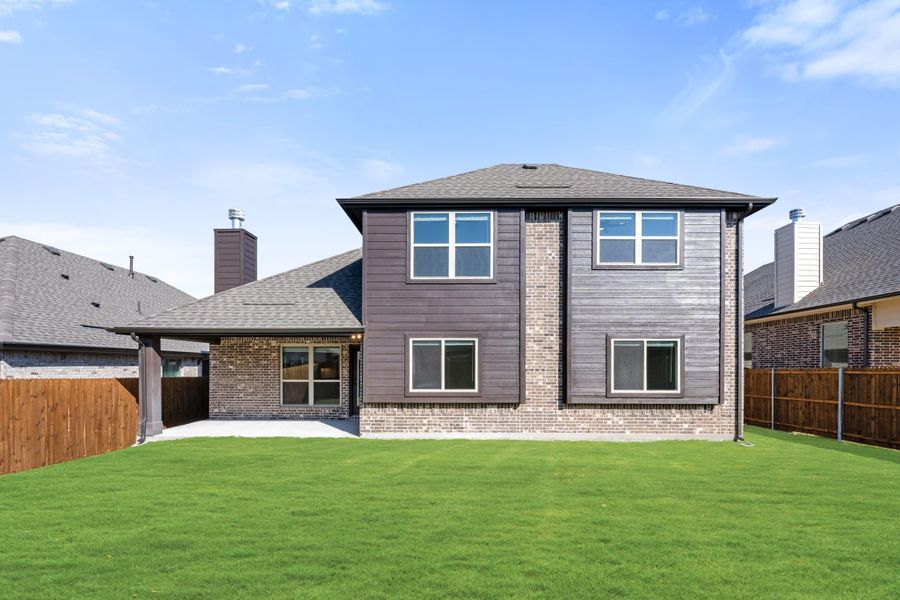 Two-story home rear view with brick and gray siding, covered patio, and fenced green backyard