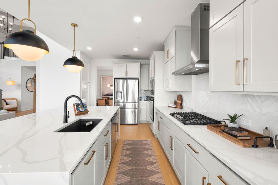 Contemporary kitchen featuring an expansive island with a matte black sink and faucet, white cabinetry with brass hardware, stainless steel appliances, and wood-finish flooring Contemporary kitchen featuring an expansive island with a matte black sink and faucet, white cabinetry with brass hardware, stainless steel appliances, and wood-finish flooring