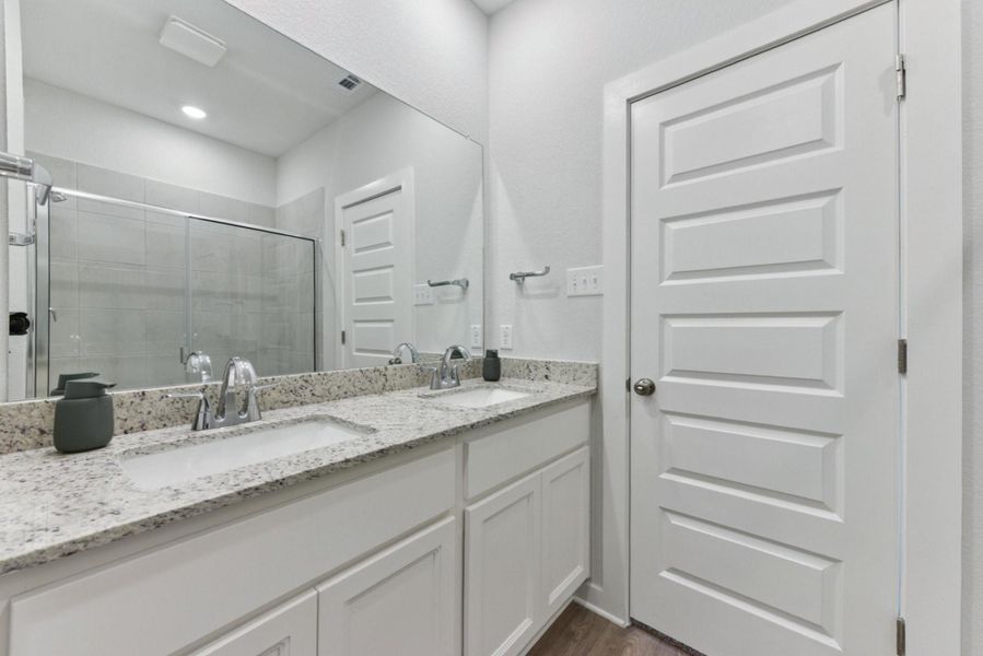 Full bathroom featuring a shower stall, double vanity, and dark wood-style flooring