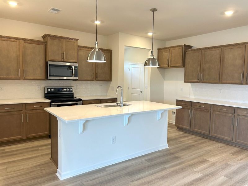 Kitchen with black electric range, stainless steel microwave, tasteful backsplash, light wood finished floors, and an island with sink