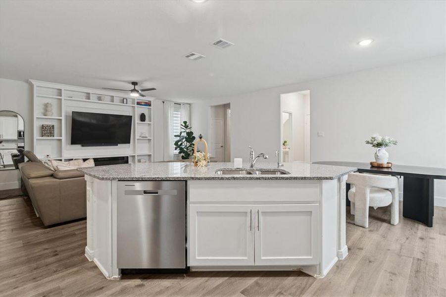 Kitchen with open floor plan, light stone counters, stainless steel dishwasher, a kitchen island with sink, and white cabinets Kitchen with open floor plan, light stone counters, stainless steel dishwasher, a kitchen island with sink, and white cabinets