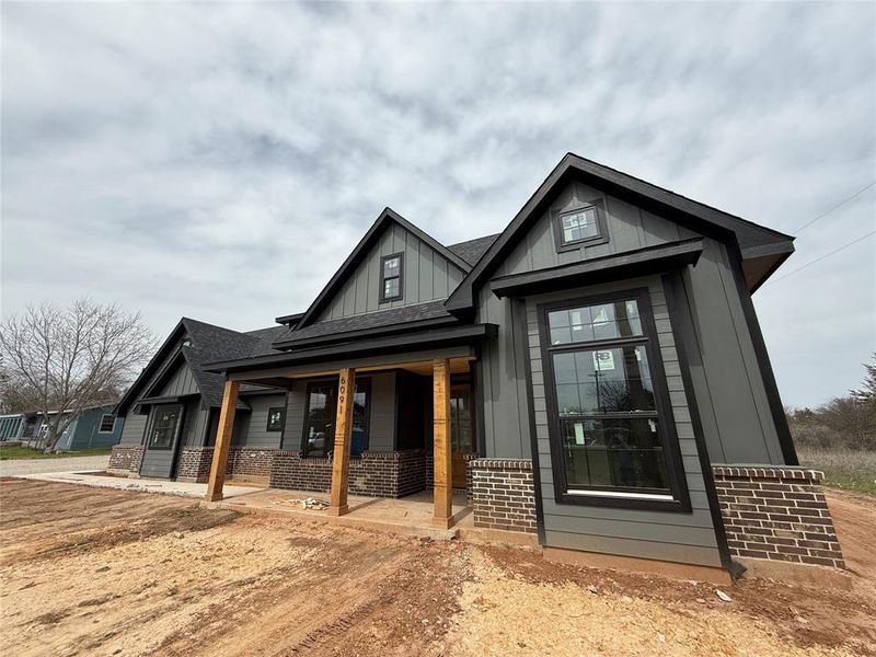 View of front of property featuring a porch, brick siding, board and batten siding, and a shingled roof