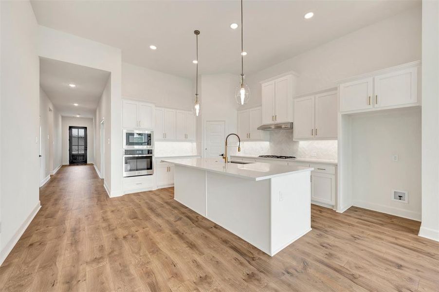 Bright kitchen featuring a substantial island with countertop seating, white shaker cabinetry, stainless steel appliances, and wood-finish flooring