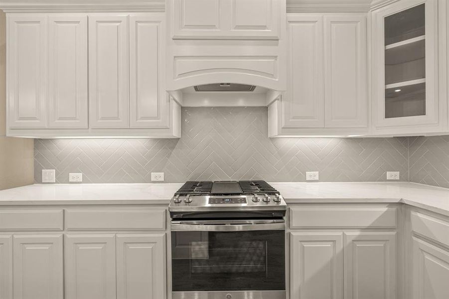 Kitchen featuring backsplash, stainless steel range with gas stovetop, and white cabinetry