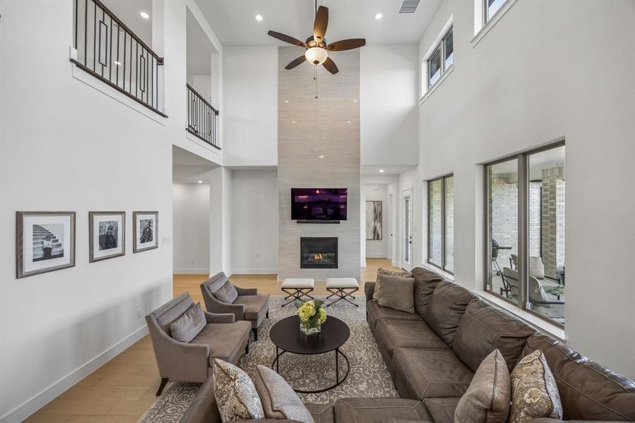 Living area with a ceiling fan, a fireplace, recessed lighting, light wood-style flooring, and a high ceiling