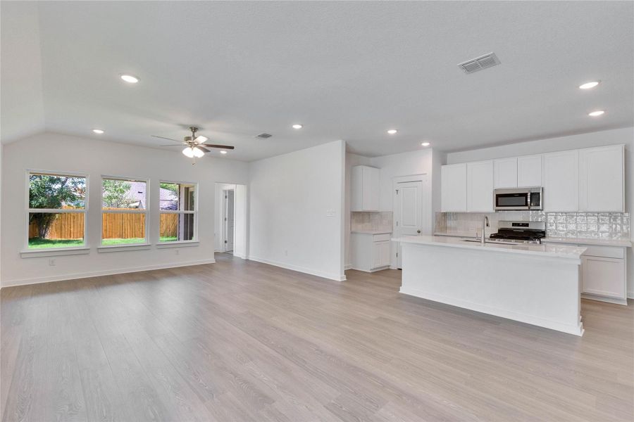 Kitchen featuring open floor plan, decorative backsplash, a kitchen island with sink, white cabinetry, and appliances with stainless steel finishes Kitchen featuring open floor plan, decorative backsplash, a kitchen island with sink, white cabinetry, and appliances with stainless steel finishes