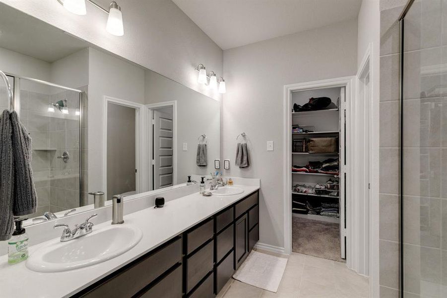 Bathroom with dual vanity, a shower with door, and tile patterned flooring