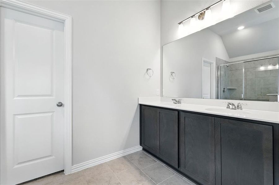 Full bathroom featuring lofted ceiling, double vanity, tiled shower, and tile patterned floors