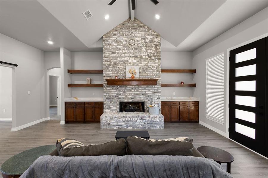 Living area with arched walkways, a brick fireplace, light wood-type flooring, beam ceiling, and a barn door