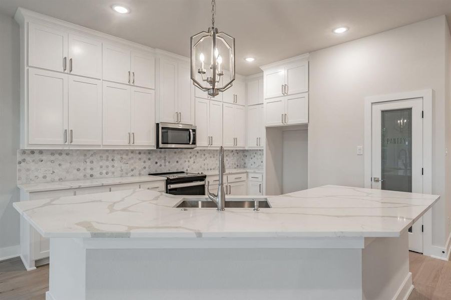 Kitchen with light wood finished floors, white cabinetry, backsplash, stainless steel microwave, and light stone counters