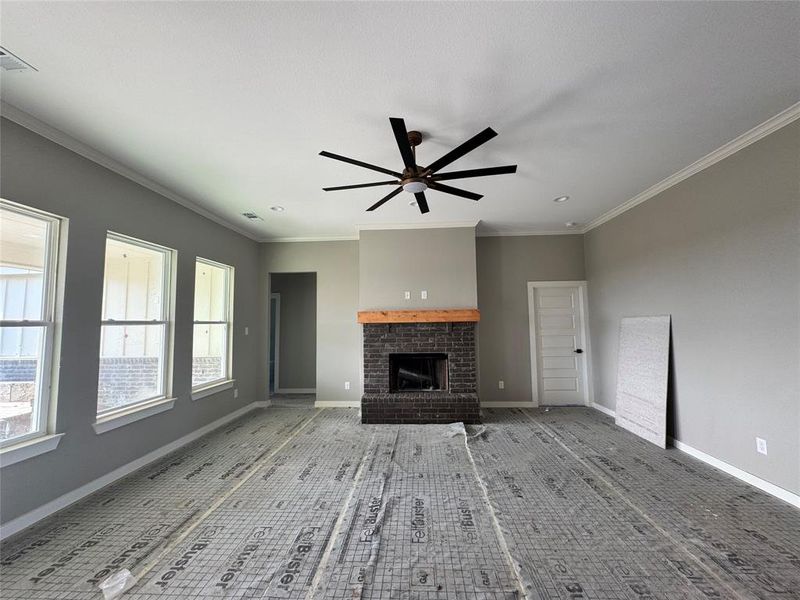 Unfurnished living room with crown molding, ceiling fan, and a brick fireplace