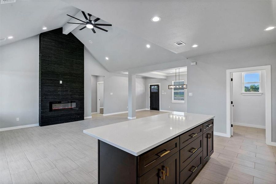 Kitchen featuring ceiling fan, lofted ceiling with beams, light hardwood / wood-style floors, a fireplace, and a kitchen island