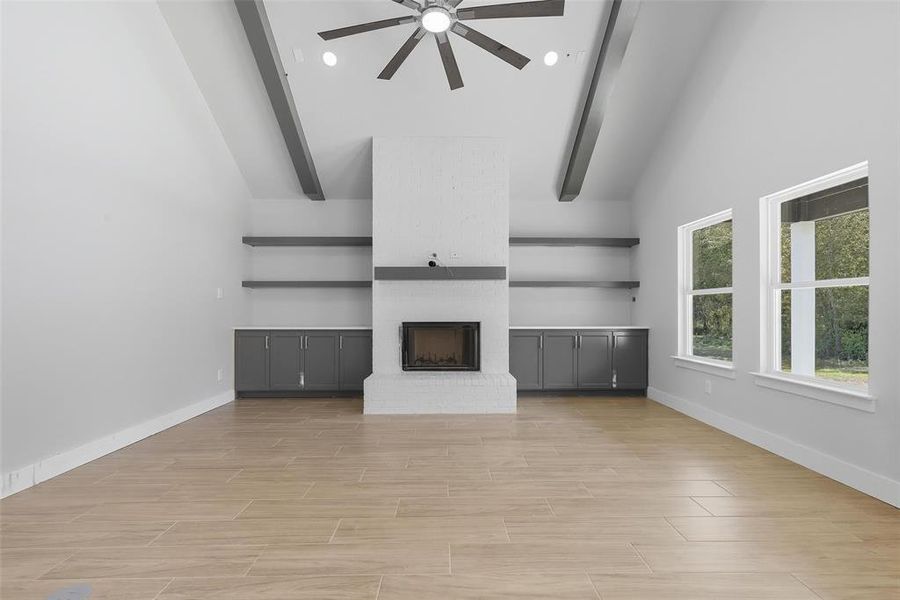 Unfurnished living room featuring a brick fireplace, high vaulted ceiling, wood finish floors, ceiling fan, and beam ceiling Unfurnished living room featuring a brick fireplace, high vaulted ceiling, wood finish floors, ceiling fan, and beam ceiling