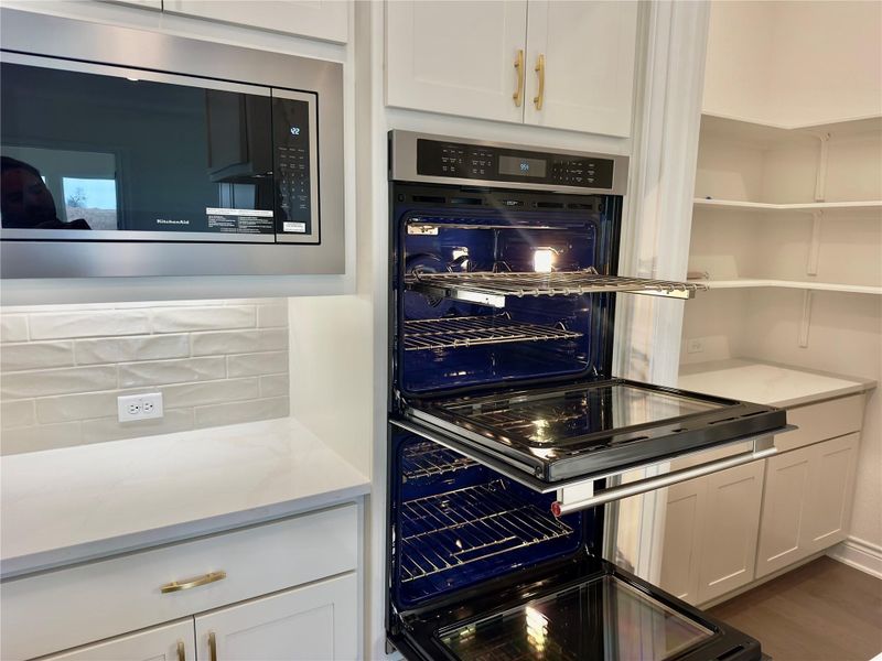 Kitchen with stainless steel appliances, white cabinetry, light stone countertops, and wood finished floors