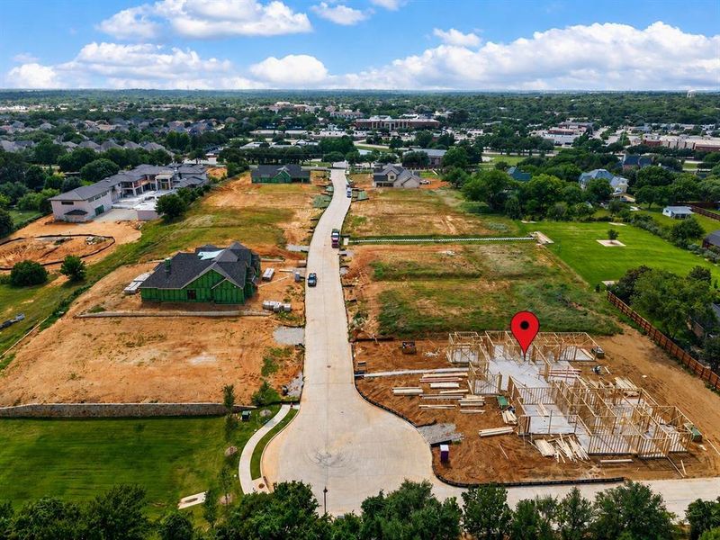 Developing residential community featuring a paved street, new home construction, and surrounding green spaces