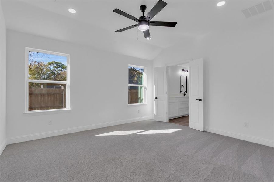 Primary bedroom with light carpet, ceiling fan, recessed lighting, lofted ceiling, and connected bathroom