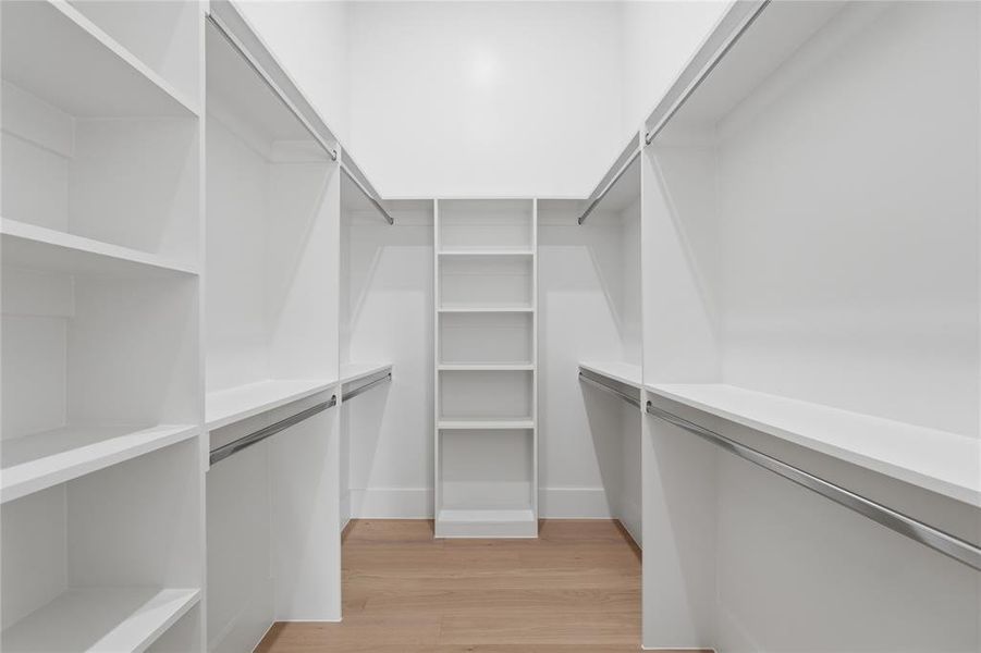 Walk-in closet featuring extensive built-in shelving, multiple hanging rods, warm wood-finish flooring, and crisp white walls Walk-in closet featuring extensive built-in shelving, multiple hanging rods, warm wood-finish flooring, and crisp white walls