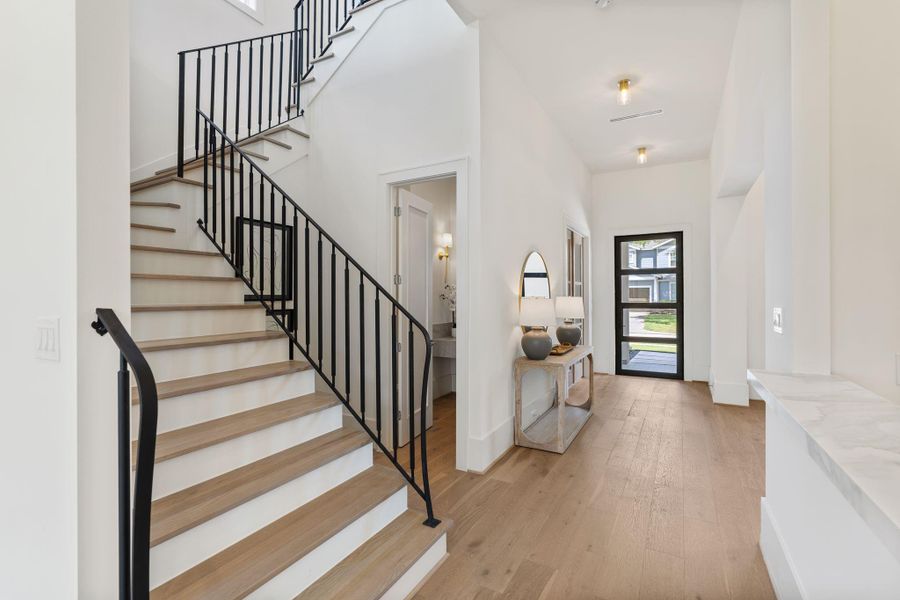 The grand entry unfolds with soaring ceilings, wide-plank white oak flooring, and a custom stair rail that makes a bold statement. Clean lines and natural light create a welcoming transition into the heart of the home.