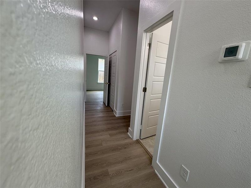 Hallway featuring wood-finish flooring, recessed lighting, and a digital thermostat Hallway featuring wood-finish flooring, recessed lighting, and a digital thermostat