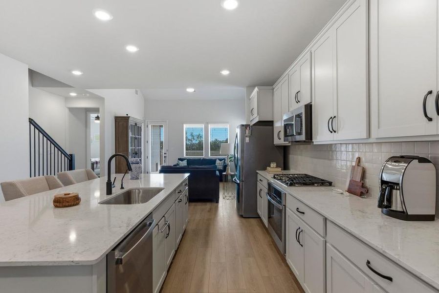 Kitchen with light stone counters, a kitchen island with sink, appliances with stainless steel finishes, open floor plan, and white cabinetry
