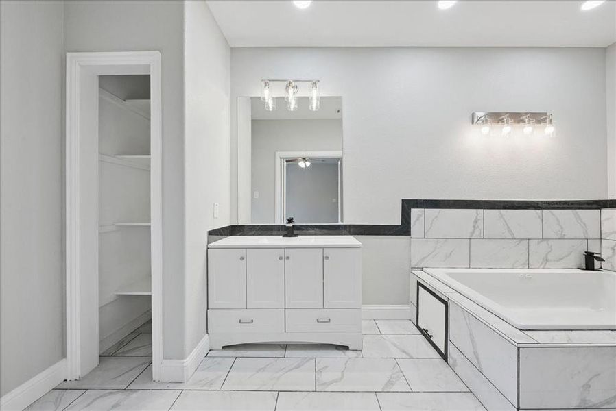 Full bath featuring vanity, a garden tub, light marble finish floors, recessed lighting, and a spacious closet