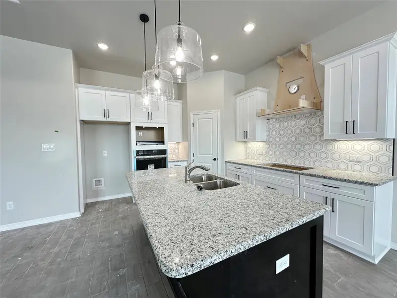 Kitchen featuring white cabinetry, light stone countertops, pendant lighting, custom range hood, and a kitchen island with sink