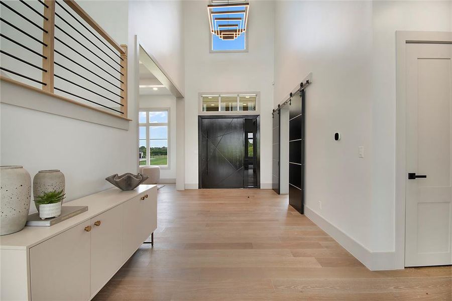 Foyer with light wood finished floors, a high ceiling, and a barn door