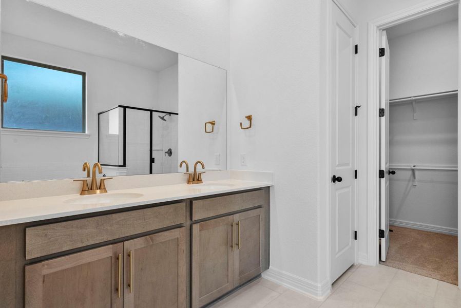 Serene and stylish primary bath with double vanity, warm stained cabinets with brass fixture, and light countertops for a relaxing retreat.