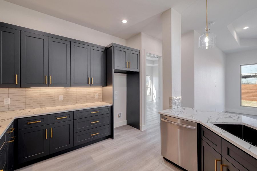 Kitchen featuring light stone counters, decorative backsplash, light wood-style floors, hanging light fixtures, and stainless steel dishwasher