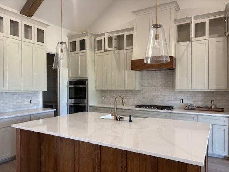 Kitchen featuring tasteful backsplash, glass insert cabinets, decorative light fixtures, light stone counters, and lofted ceiling