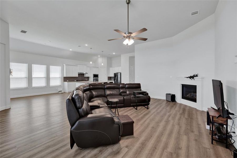 Living room featuring light wood-style flooring, a ceiling fan, a glass covered fireplace, and recessed lighting