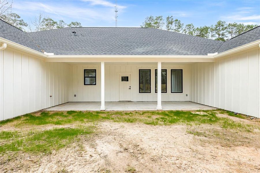 This photo shows a spacious covered patio with a concrete floor and a view of a large, partially fenced backyard with trees, offering a great outdoor living space.