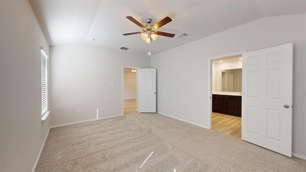 A spacious bedroom features a ceiling fan, carpet, and a view into the adjoining primary bathroom.