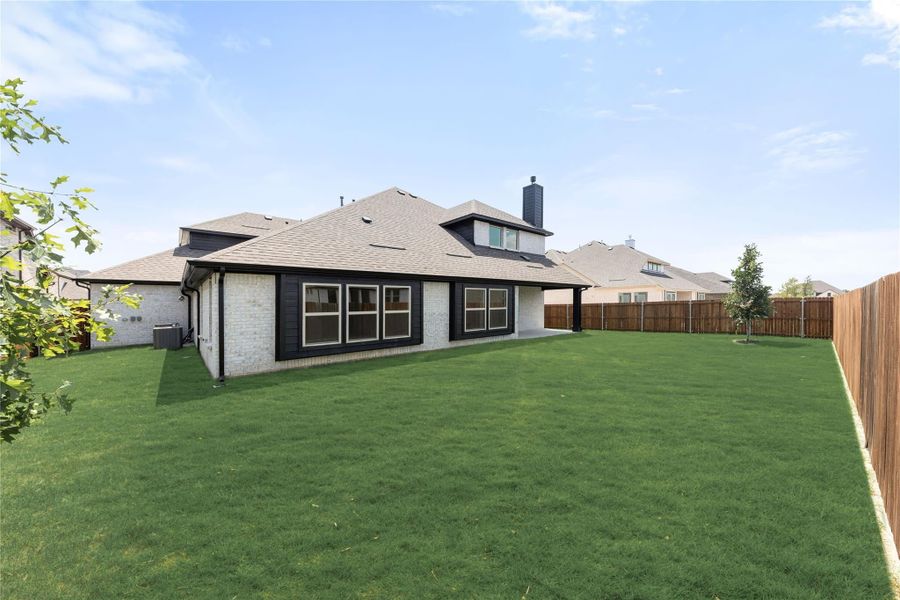 Rear view of single-story brick home with large fenced backyard, covered patio, and chimney Rear view of single-story brick home with large fenced backyard, covered patio, and chimney