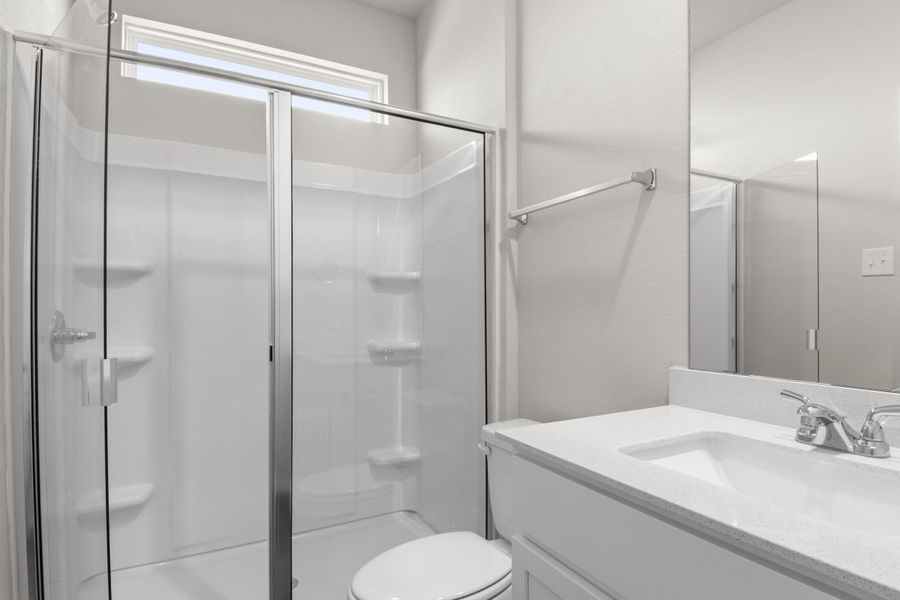 A bathroom with white vanity with white countertops, a mirror, and a walk-in glass shower, and white toilet.