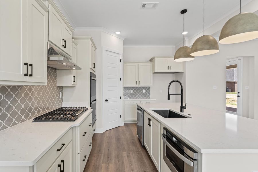 Kitchen with a center island with sink, light stone countertops, hanging light fixtures, dark wood finished floors, and ornamental molding Kitchen with a center island with sink, light stone countertops, hanging light fixtures, dark wood finished floors, and ornamental molding