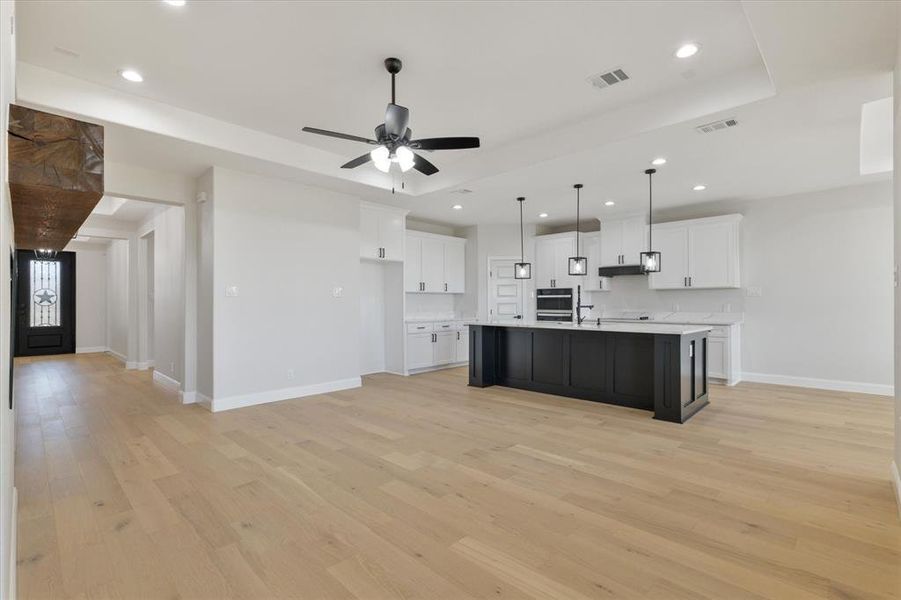 Kitchen featuring light wood finished floors, a center island with sink, white cabinets, open floor plan, and light countertops