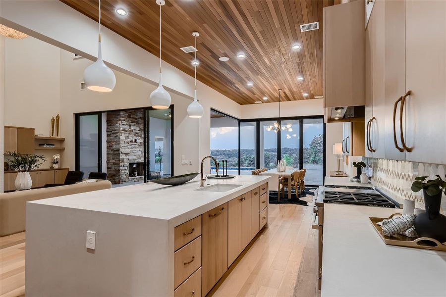 Well-appointed kitchen featuring a large island with a sink, light-colored countertops, and light wood cabinetry