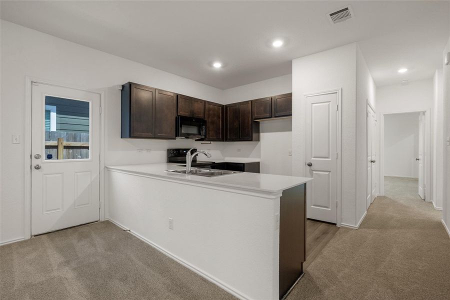 Kitchen featuring black microwave, light colored carpet, dark brown cabinets, a peninsula, and recessed lighting Kitchen featuring black microwave, light colored carpet, dark brown cabinets, a peninsula, and recessed lighting