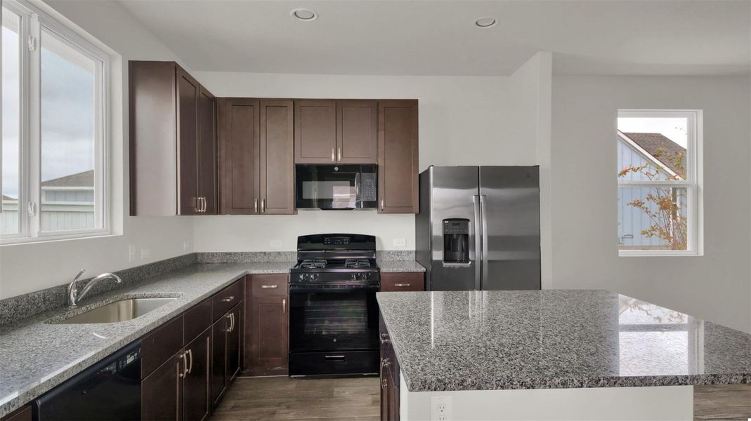 Kitchen with black appliances, light stone countertops, a kitchen island, dark wood finish cabinetry, and light wood-type flooring