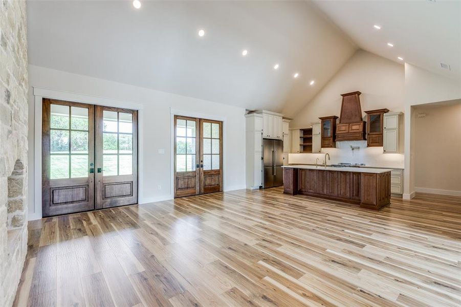 Kitchen with an island with sink, high vaulted ceiling, french doors, and a custom range hood