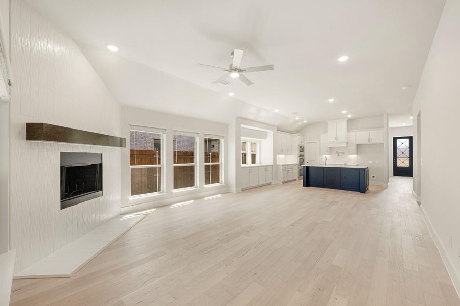 Open-concept living area with fireplace, ceiling fan, and kitchen featuring navy island and white cabinets with light hardwood floors