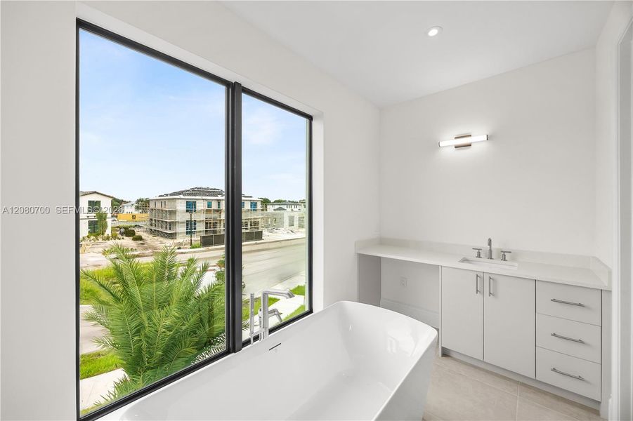 Freestanding soaking tub, large format window, single vanity with integrated sink, quartz countertop, and vanity lighting