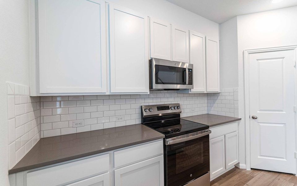 Kitchen with stainless steel appliances, white cabinetry, decorative backsplash, and light wood-type flooring