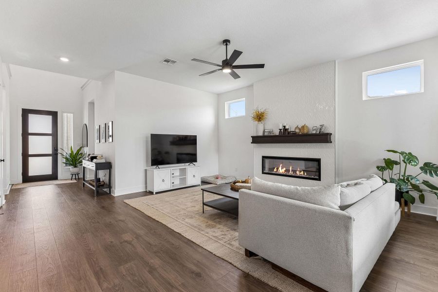 Rich hardwood flooring complements a modern linear fireplace under elevated ceilings.